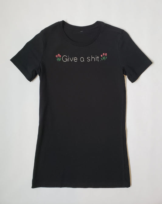 A slim fit black crew neck tee with "Give a shit" hand embroidered in white, in a font similar to Helvetica. Three tulips are on either side of the text. The tulips are gathered together like they are planted alongside the text. They are a muted red.